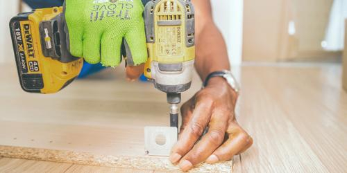 A person holds a drill and uses it on a piece of wood.